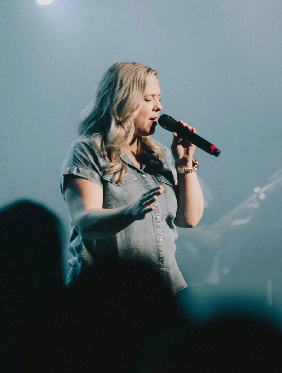 A worship leader singing with her eyes closed on a softly lit stage
